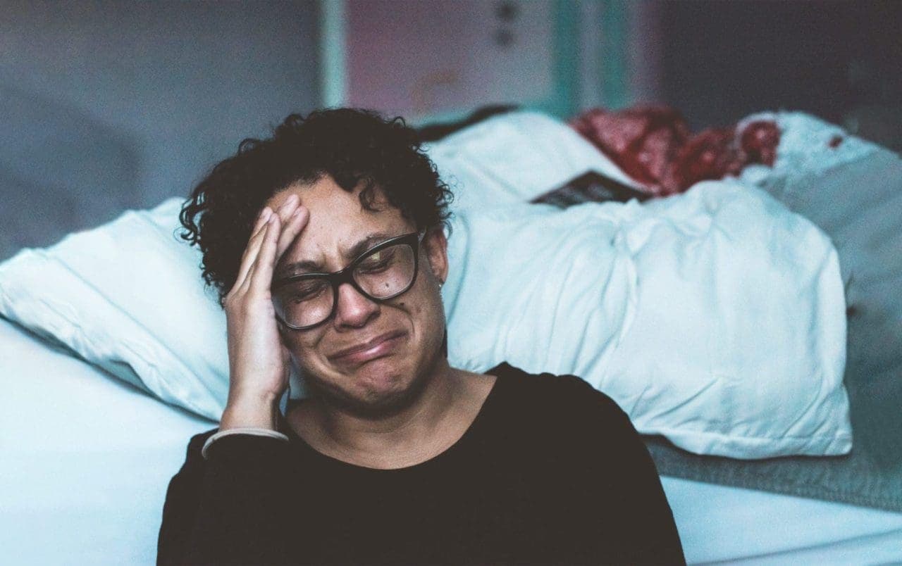 man wearing eyeglasses holding his side forehead and crying
